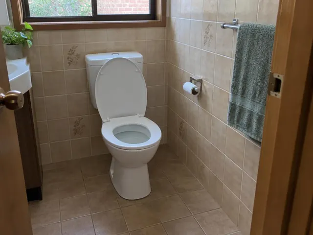 Clean white toilet in a beige tiled bathroom with a towel rail and window in Allambie Heights