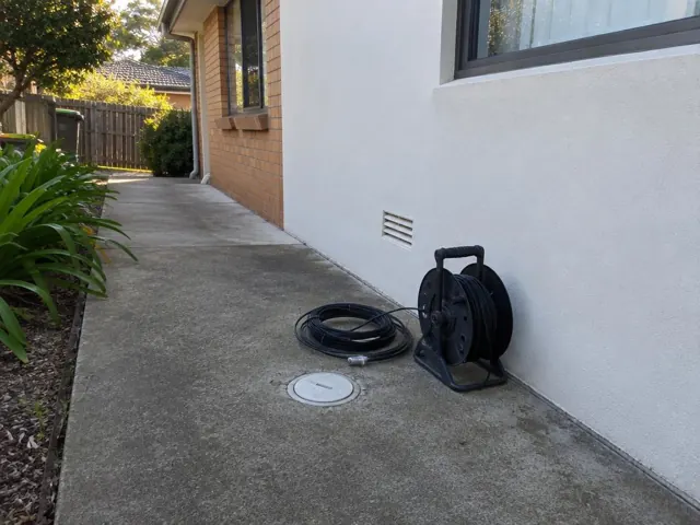 Capped drain inspection opening with camera reel on a concrete side path beside a house in Frenchs Forest